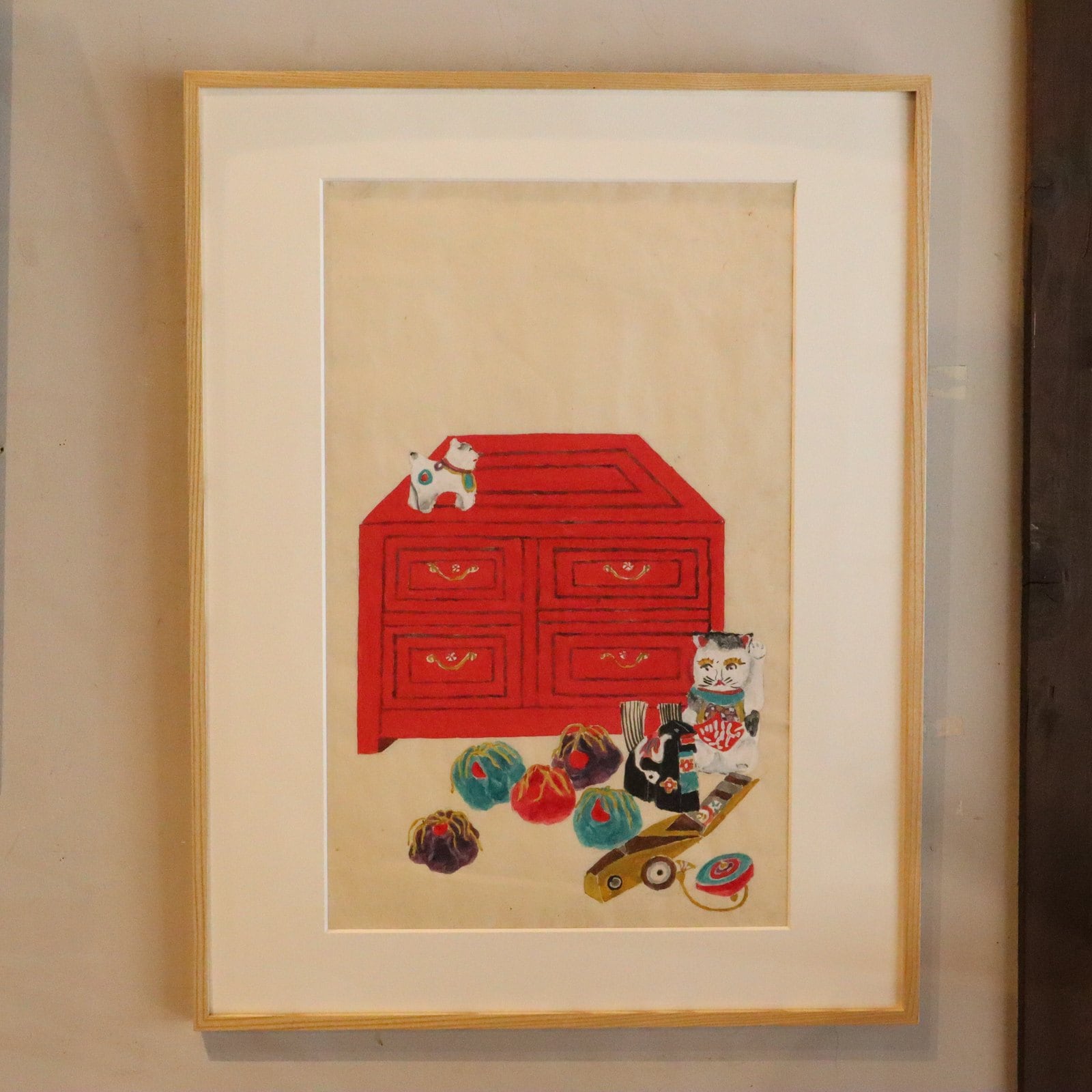 赤い箪笥と招き猫、手毬などを描いた額装の作品