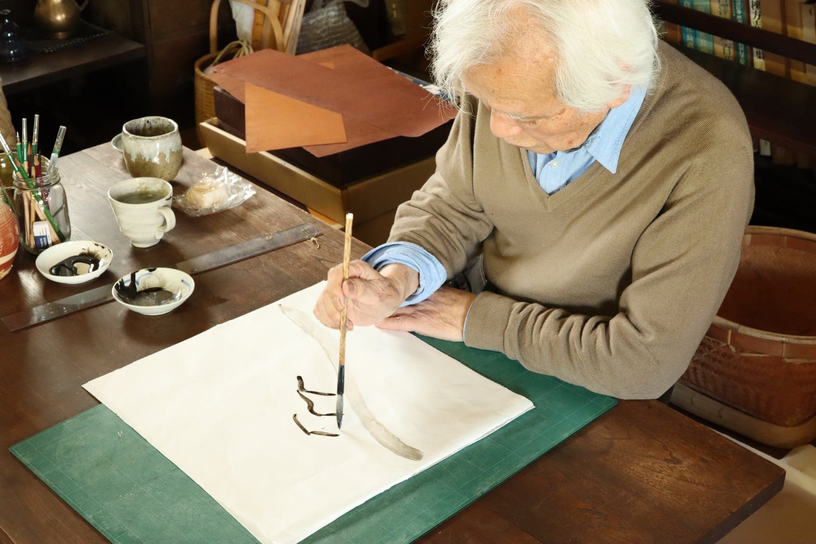 机に広げた紙に、筆で図案を描く下平先生