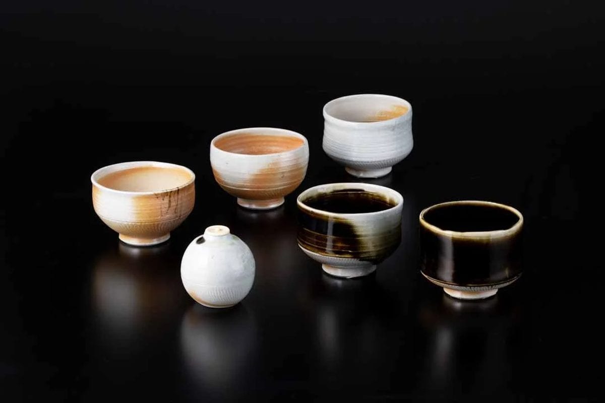 Cups and small bowls with white, amber and dark glazes on a black surface
