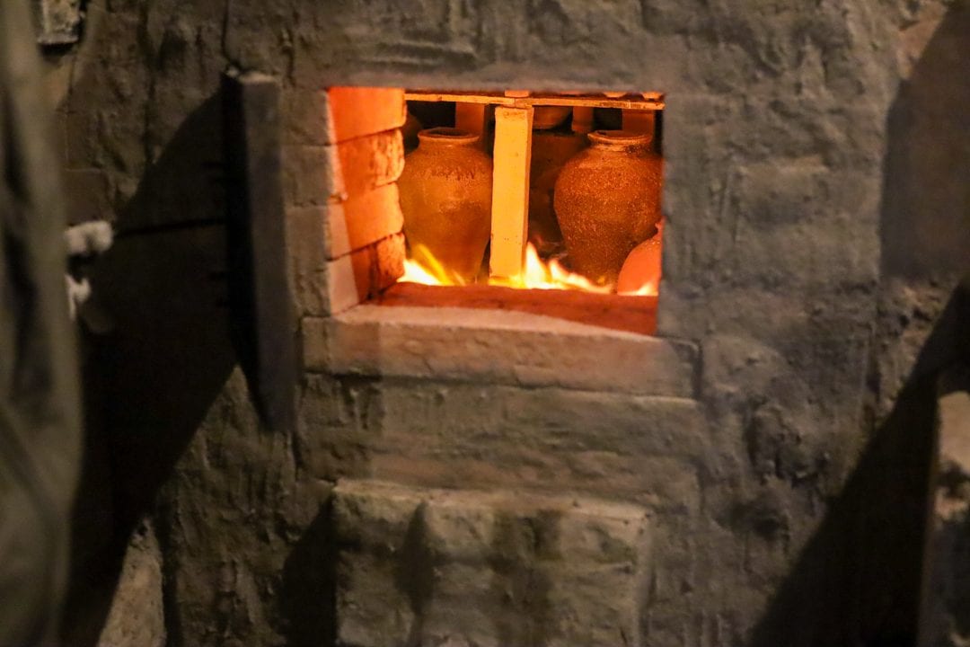Jars glowing orange inside a kiln during firing, seen through a stoke hole in the kiln wall