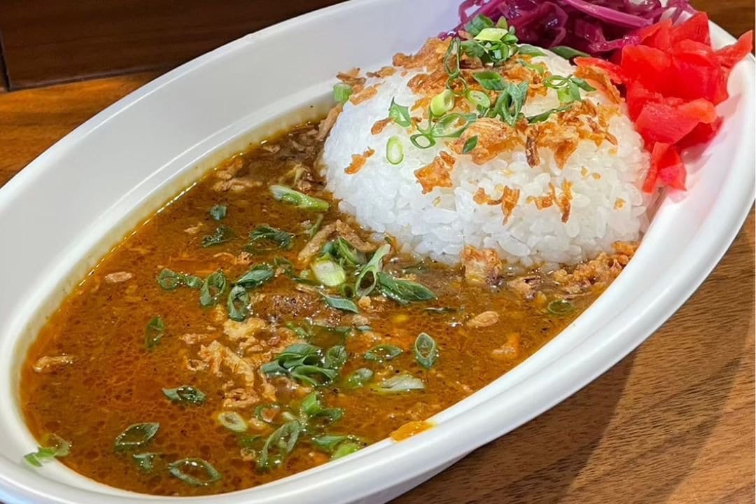 A plate of curry and rice topped with spring onions and pickled ginger