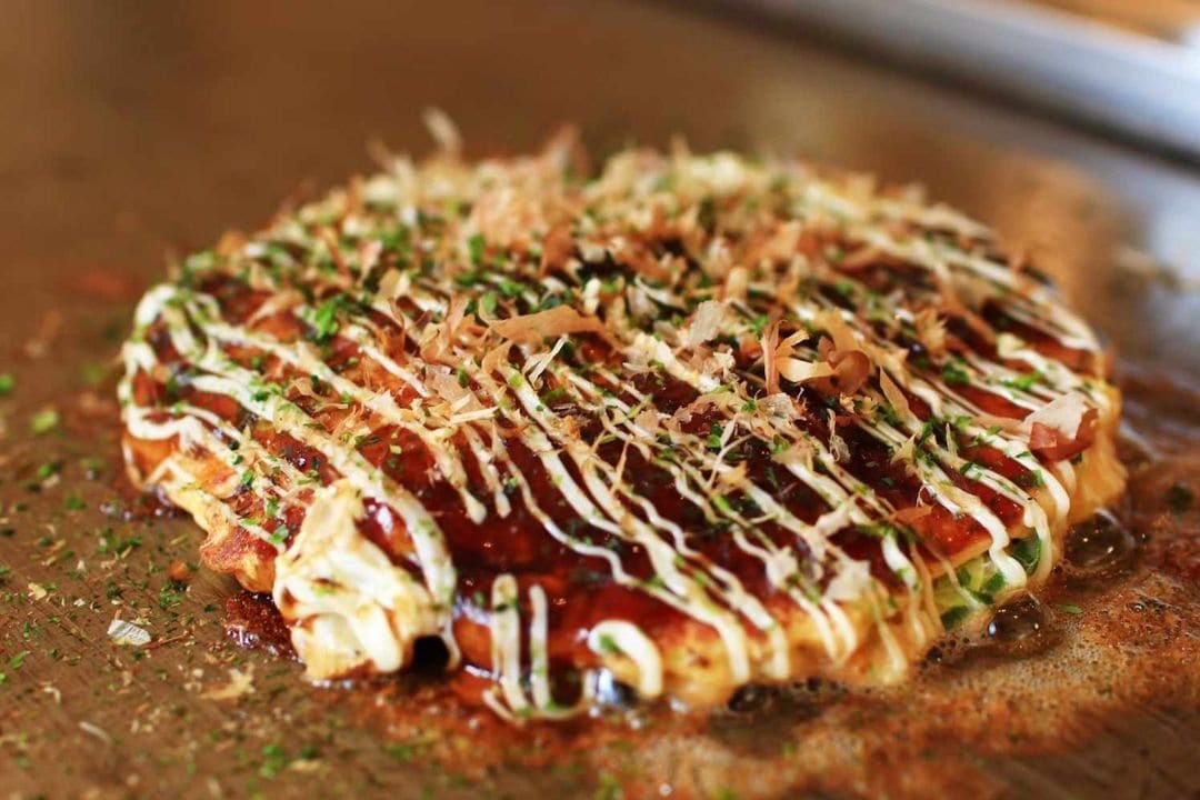 Okonomiyaki topped with mayonnaise, sauce and bonito flakes